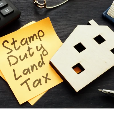 Close-up of sticky note on desk: "Stamp duty land tax" next to house model.